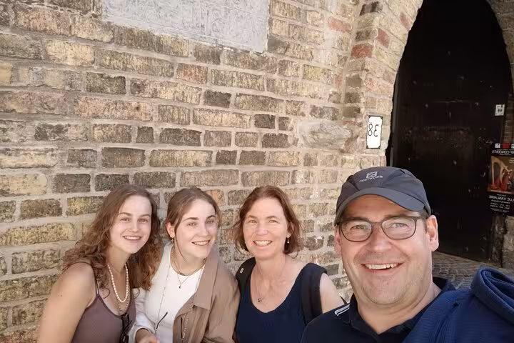 Family of four smiling in front of historic brick archway gate in Bruges