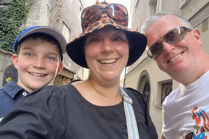 Family of three smiling on a selfie during a walking tour through Salzburg Old Town narrow streets