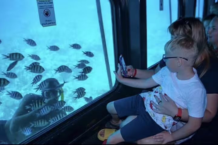 Family inside Hurghada semi submarine watching Red Sea fish through glass window on snorkeling sea trip tour