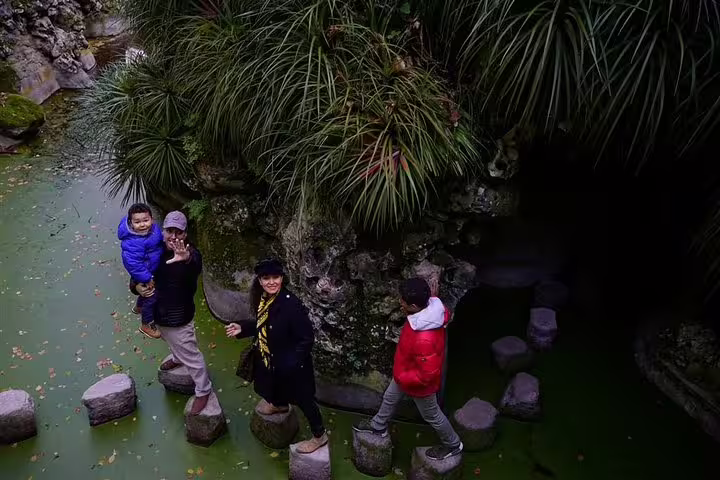 Family enjoying a private Sintra tour from Lisbon, exploring lush gardens and stepping stones near historic monuments.