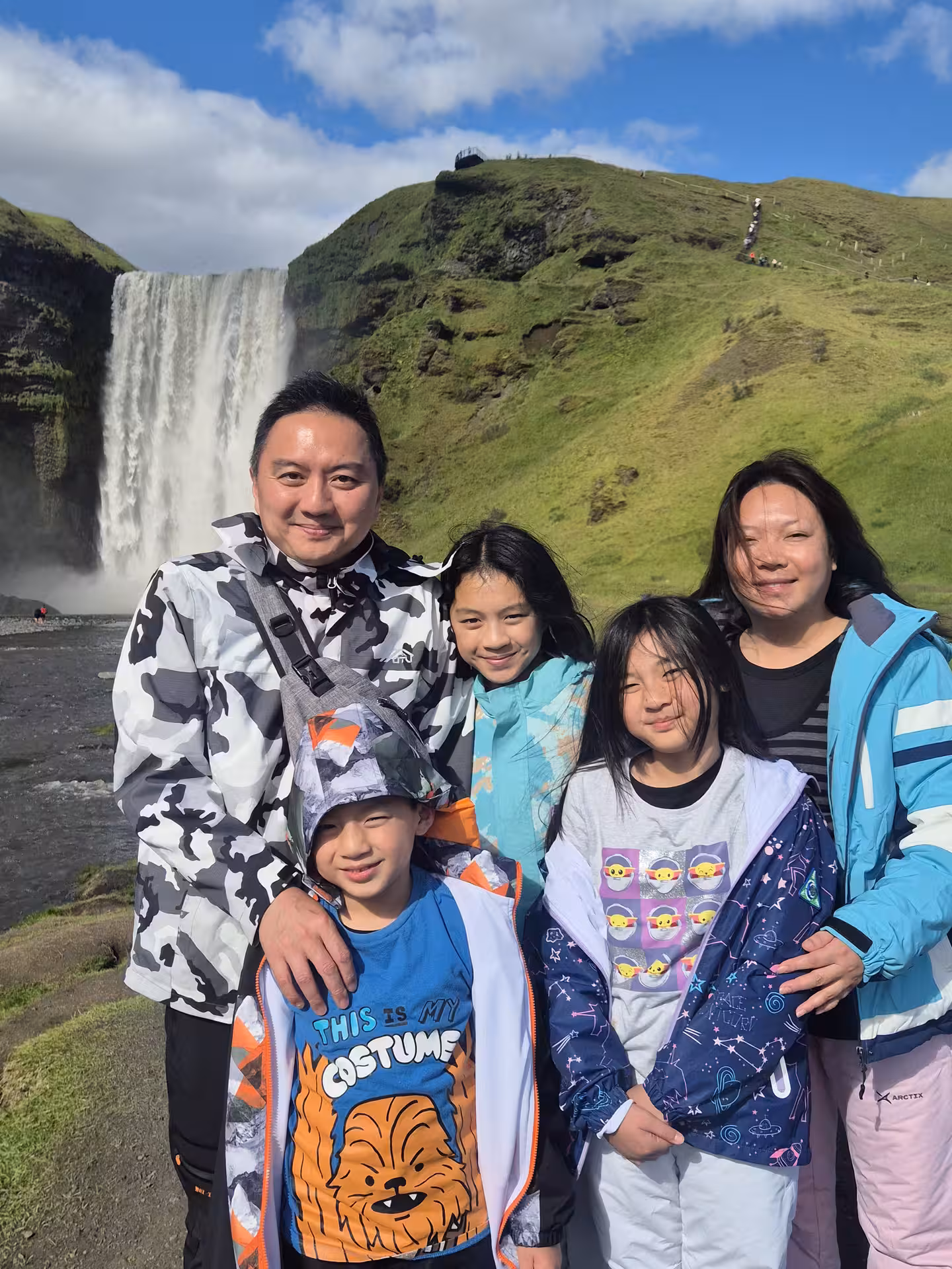 Family of five smiling in front of Skógafoss waterfall on Iceland's South Coast