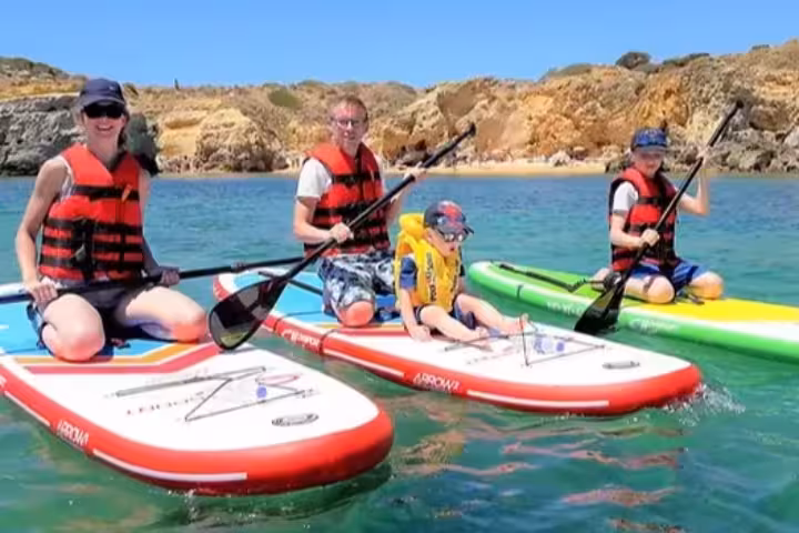 Family enjoying a private SUP paddleboard tour near Albufeira caves wearing life jackets on colorful boards