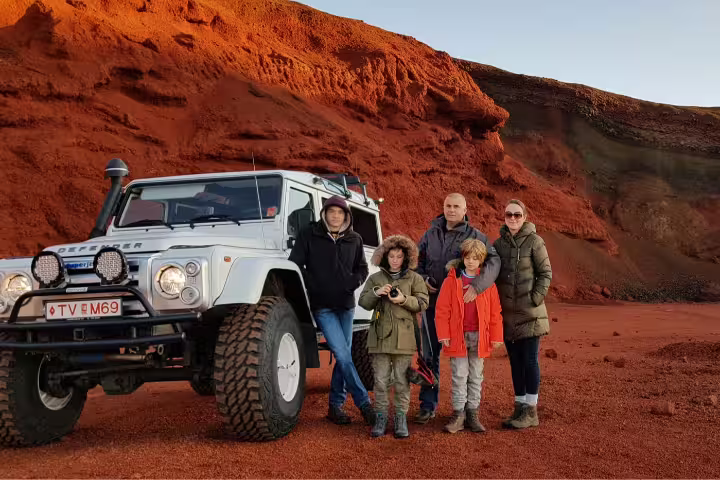 Family posing beside a rugged superjeep in Iceland's red volcanic landscape during the Silfra Golden Circle Snorkeling Tour.