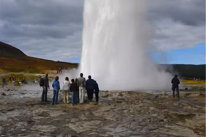 Tourists watching Strokkur geyser eruption in Iceland on a cloudy summer day