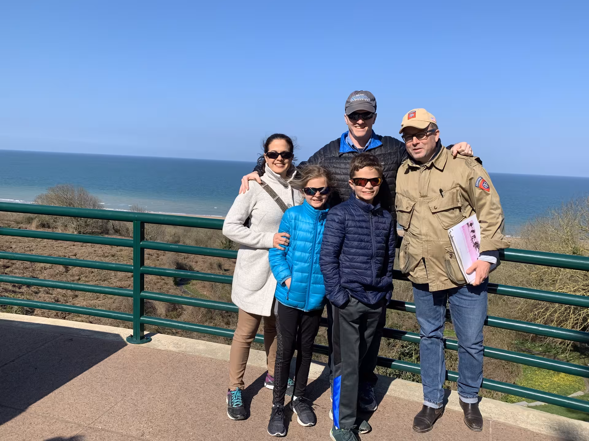 Family group posing at scenic Normandy D-Day beach overlook on a clear sunny day