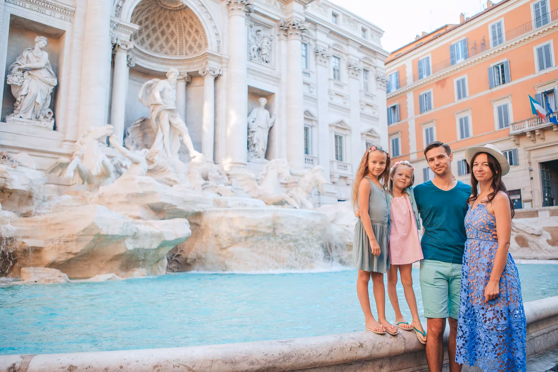 Family of four posing at the Trevi Fountain in Rome on a sunny day