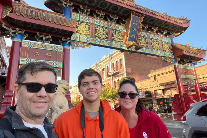 Family selfie at Victoria Chinatown Gate on a city highlights scavenger hunt walking tour in Victoria BC