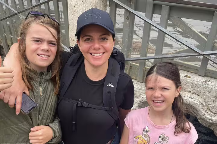 Woman with backpack and two children smiling together outdoors on a walking tour