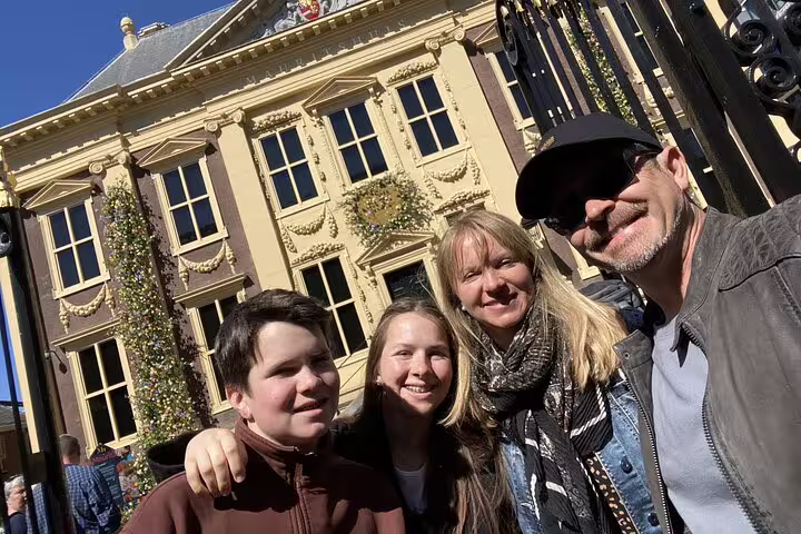 Family posing for selfie in front of historic yellow Mauritshuis building in The Hague old town