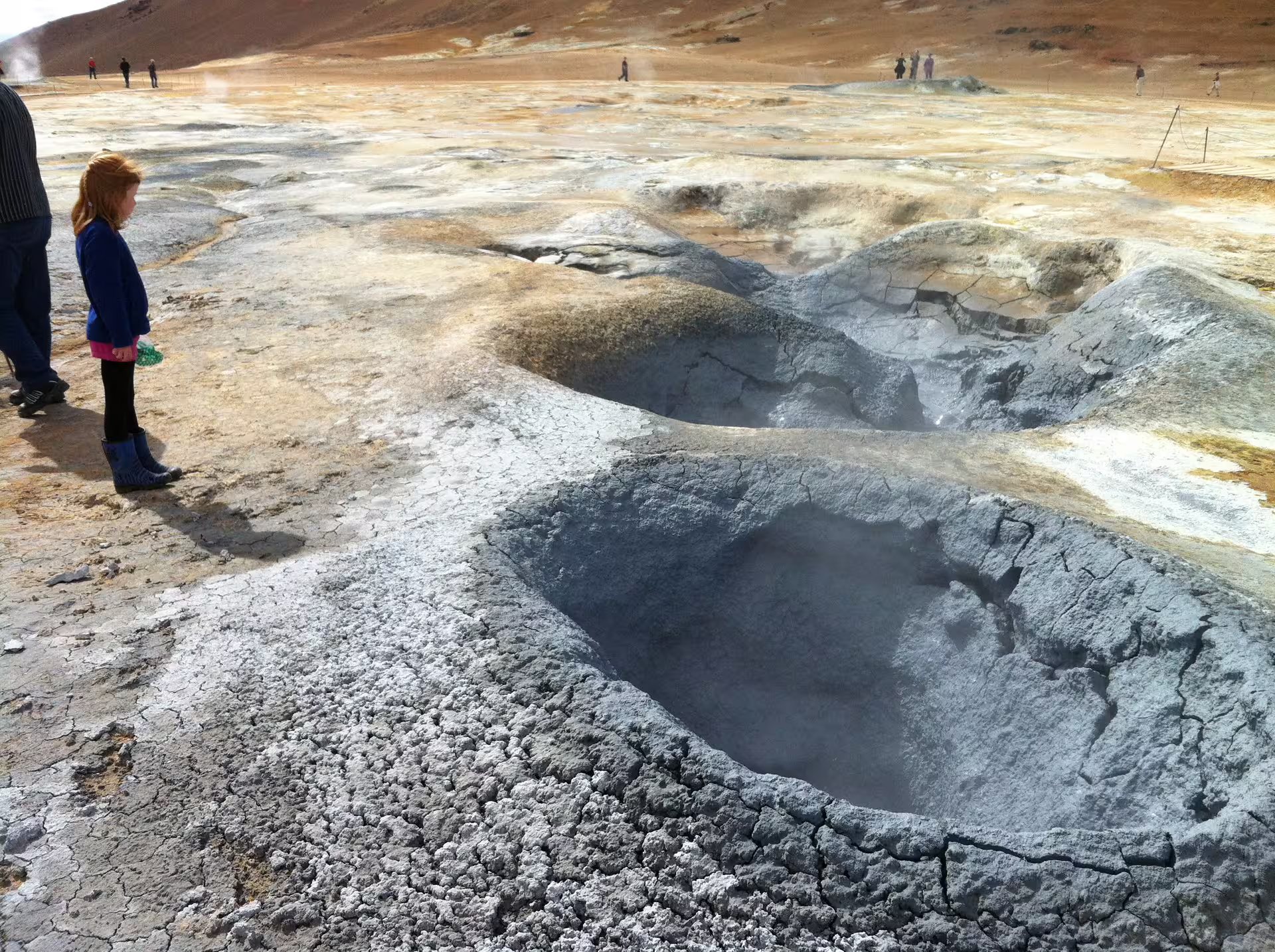 Young girl observing steaming geothermal mud pools at Hverir volcanic area in Iceland