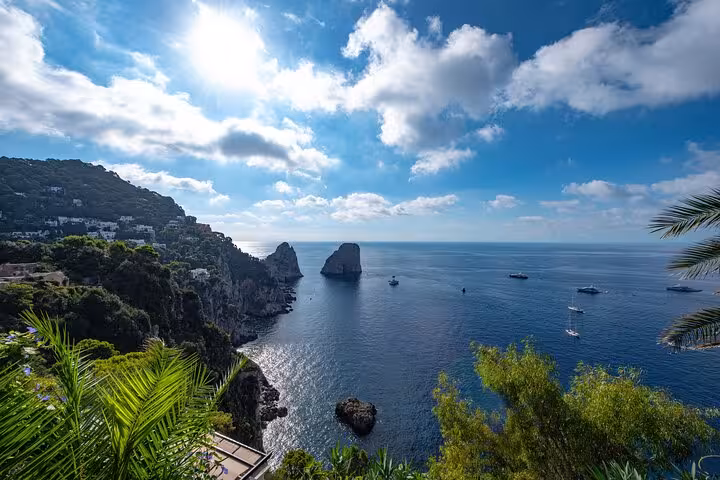 Stunning view of the Faraglioni rock formations in Capri with lush greenery and boats under a vibrant sky.