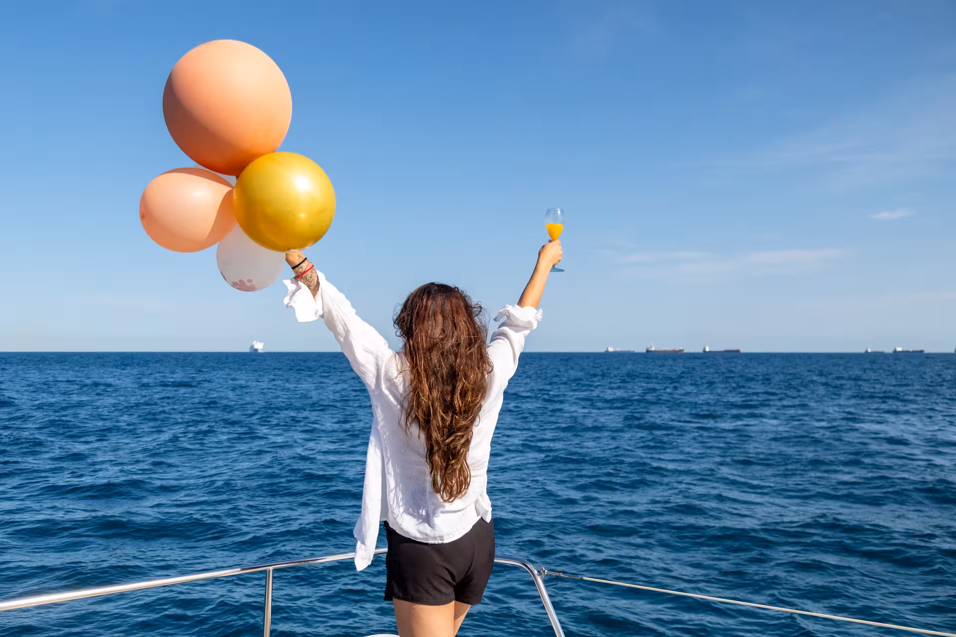 Guest on Farewell at Sea yacht cruise raises champagne and balloons over the open ocean on a sunny day