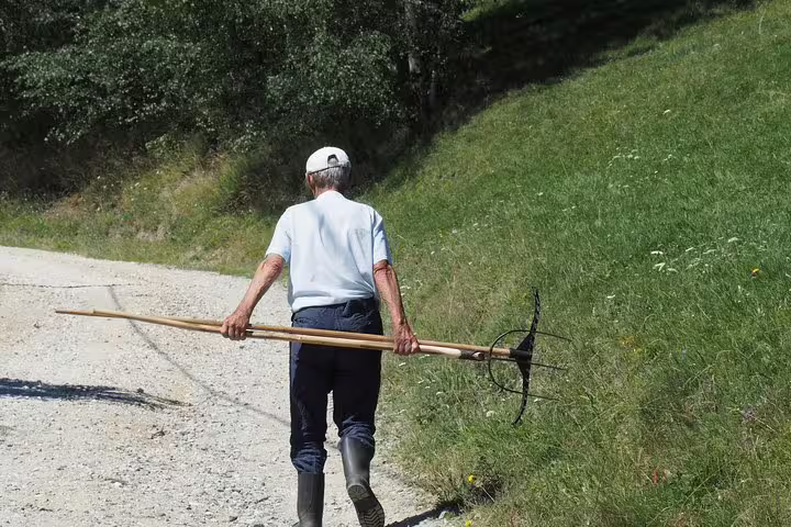 Elderly farmer carrying a pitchfork along a rural mountain village path in Romania