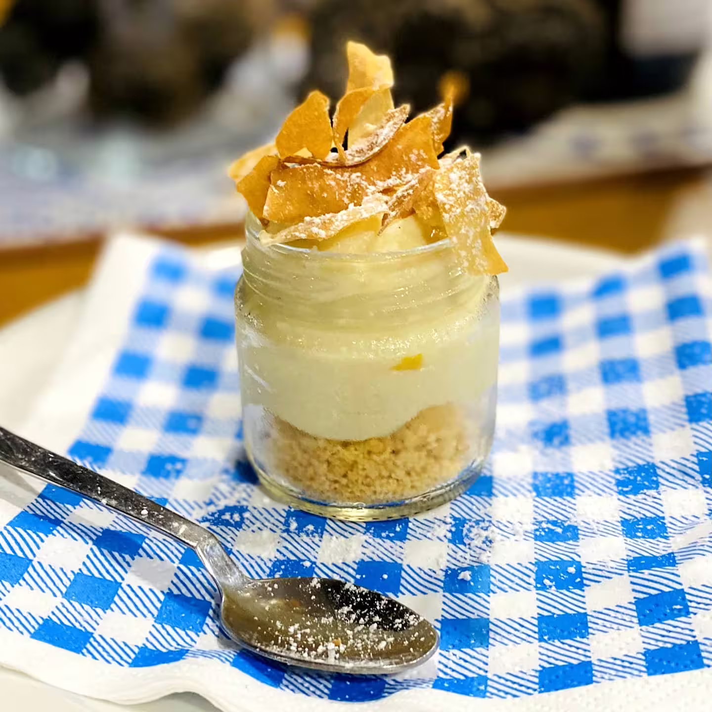 Creamy farmhouse dessert in a glass jar with biscuit crumble, served on a blue checkered napkin during vineyard tasting experience