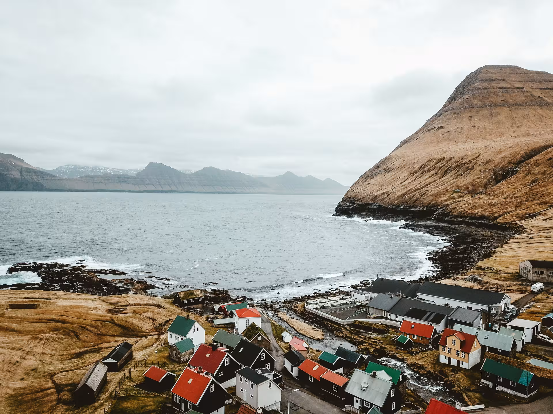 Colorful village houses along the rocky coastline of the Faroe Islands with dramatic cliffs and fjord views