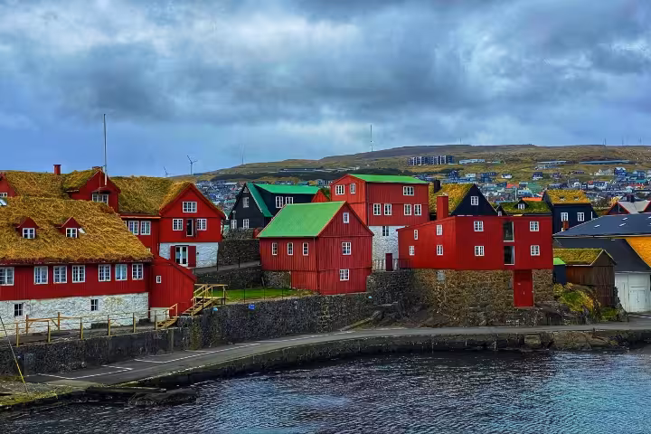 Red wooden houses with grass roofs along the waterfront in the Faroe Islands under cloudy skies