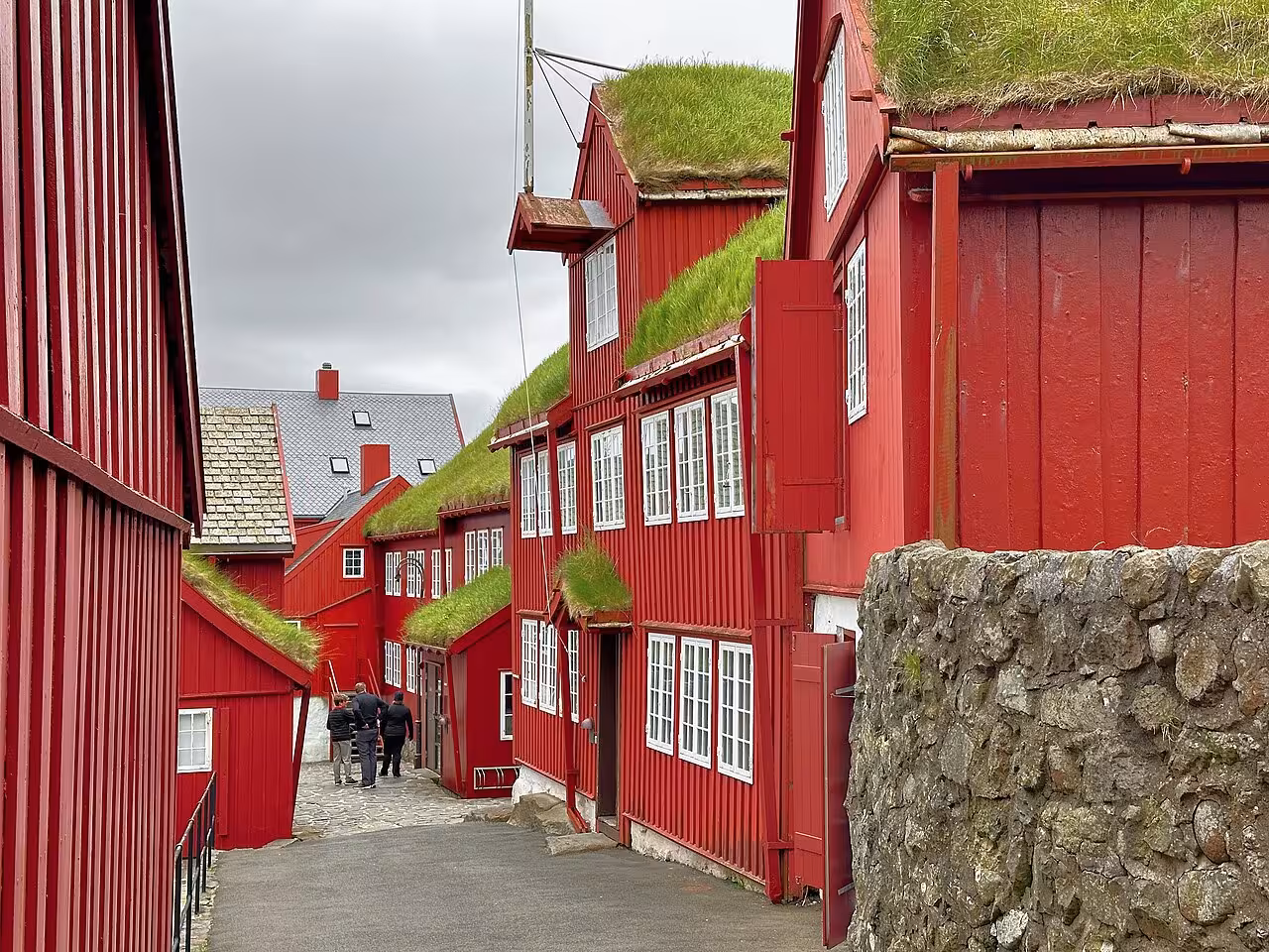 Red wooden buildings with grass sod roofs lining a narrow cobblestone street in the Faroe Islands