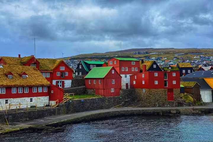 Red wooden buildings with grass-covered roofs along the waterfront in the Faroe Islands under cloudy skies