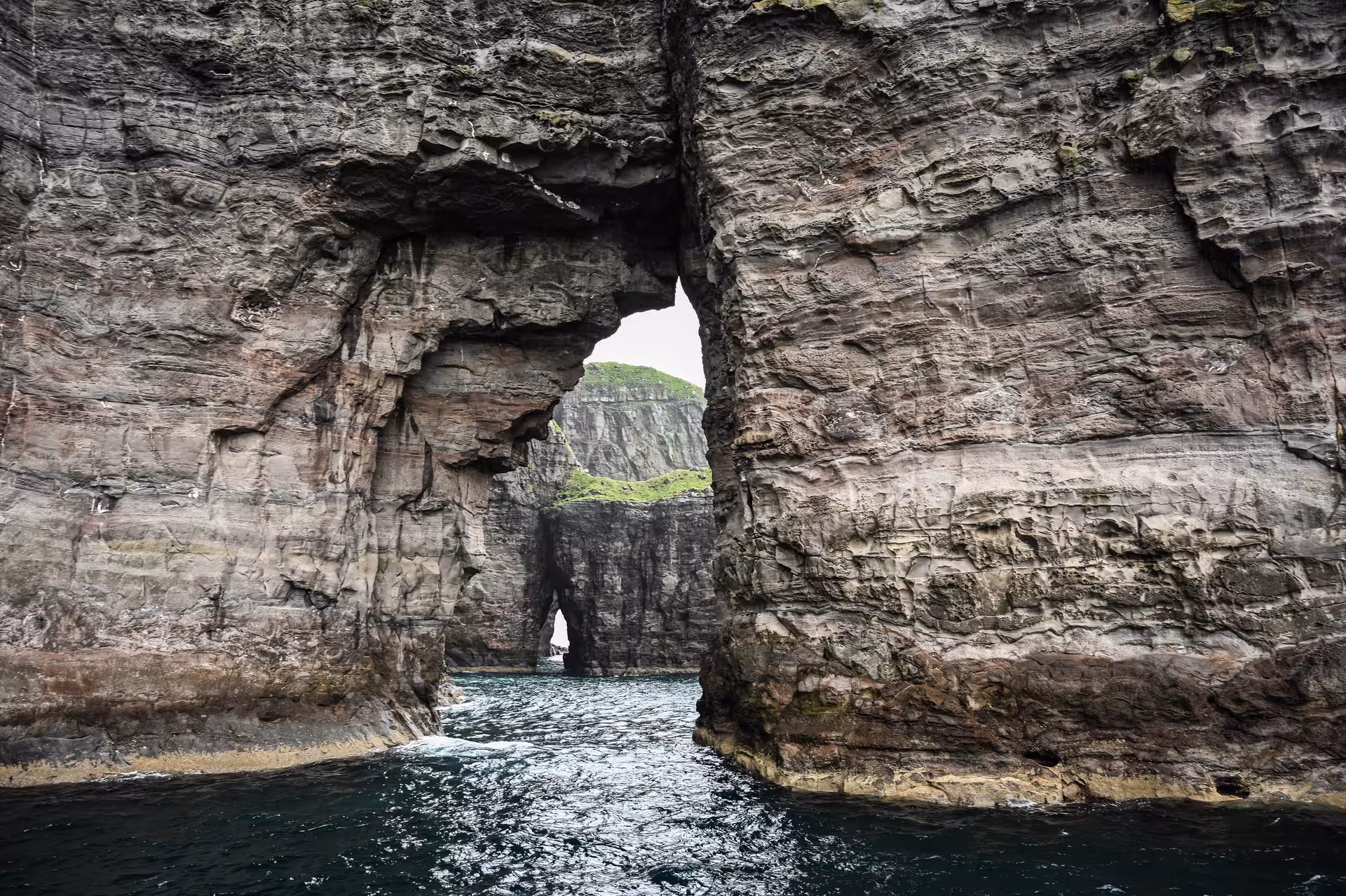 Natural rock sea arch with layered cliffs and dark waters in the Faroe Islands