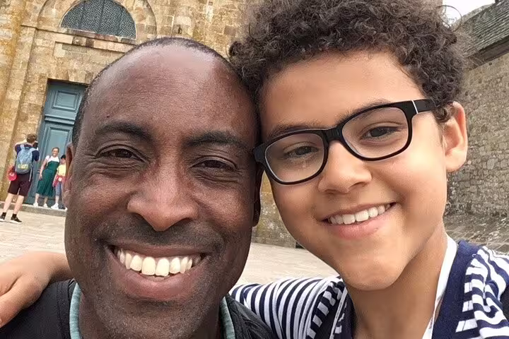 Smiling man and boy with glasses taking selfie at Mont Saint-Michel Abbey stone walls