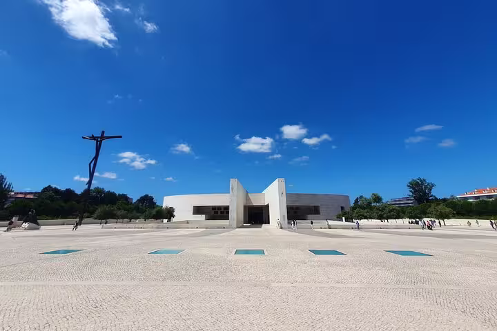 Visit the modern architecture of the Fátima Basilica, featuring a striking crucifix under the clear blue sky.