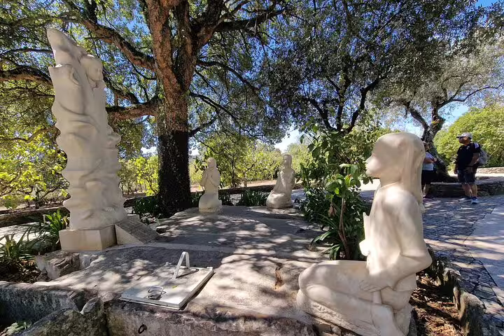 White marble statues under lush trees at a serene outdoor setting, part of the Fatima and Portugal caves private tour from Lisbon.