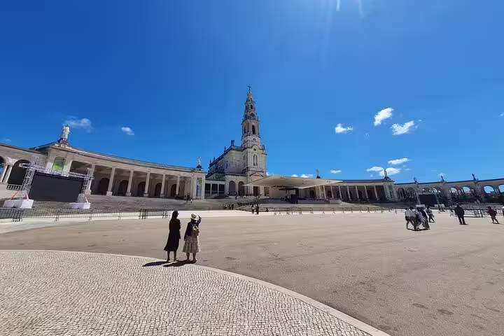 Visitors admire the stunning architecture of the Sanctuary of Fátima under a clear blue sky on a private tour from Lisbon.