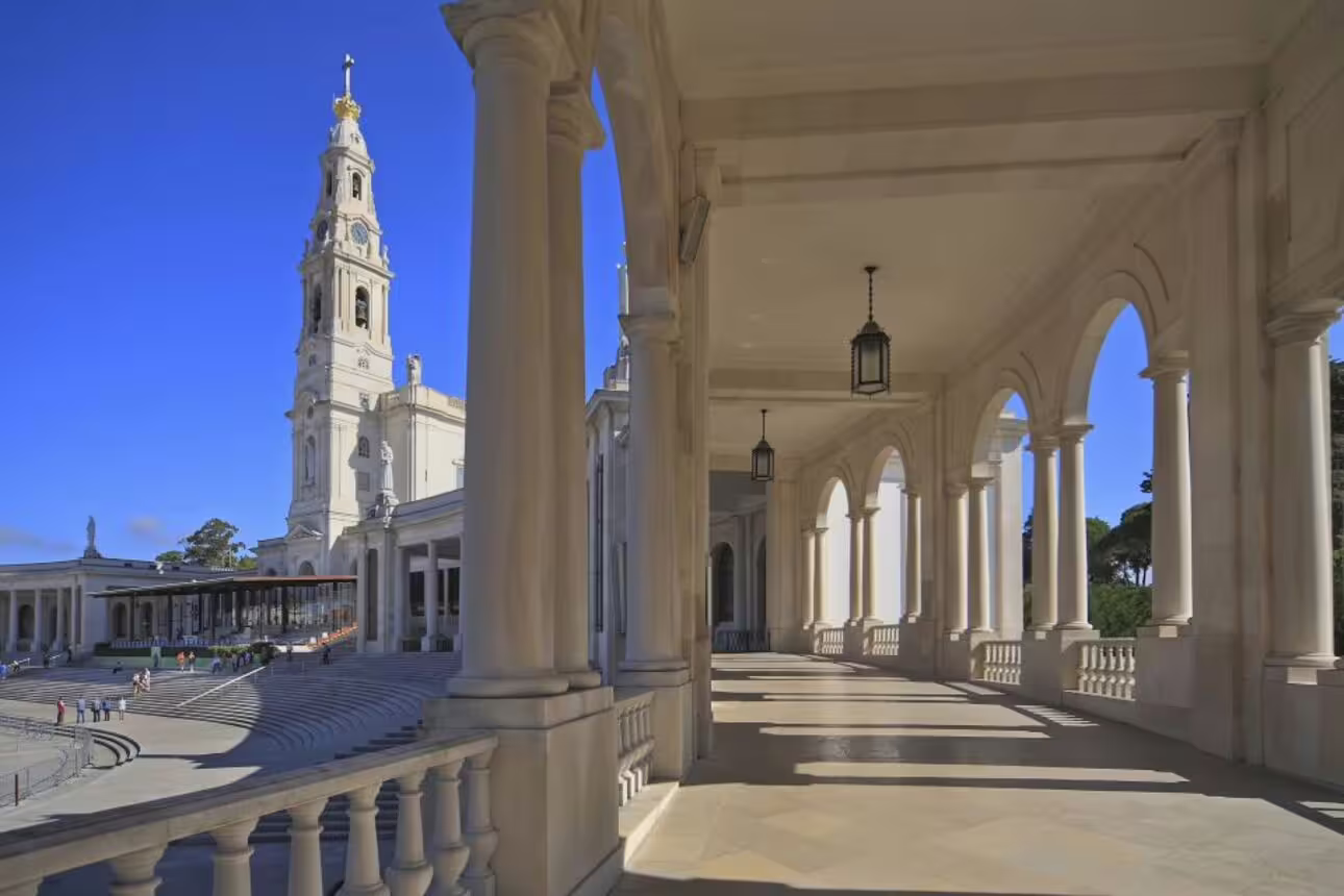 View of the Sanctuary of Fátima's colonnade and bell tower on a clear day, featured in guided tours from Lisbon.