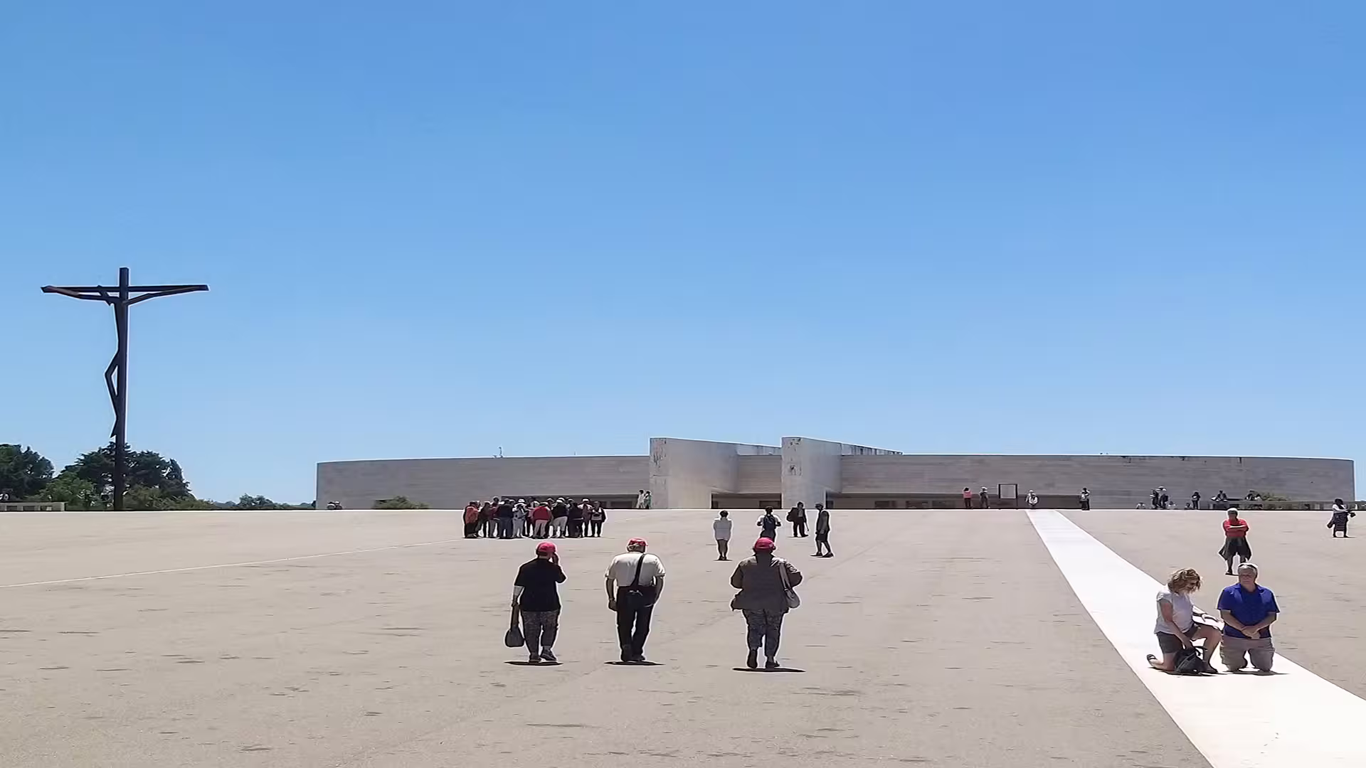 Visitors exploring the expansive courtyard at Fátima Sanctuary, with a modern cross under a clear blue sky, during a private tour.