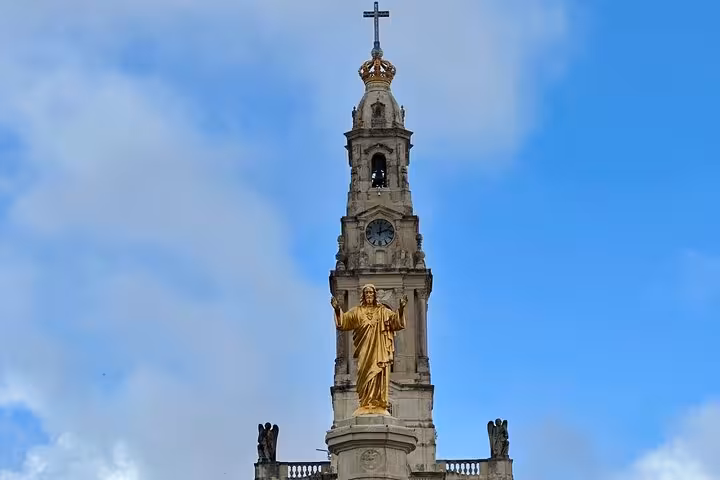 View of the Sanctuary of Fátima with its iconic golden statue and bell tower against a clear blue sky.