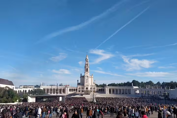 Visitors gather at the Sanctuary of Fátima under a clear blue sky, a highlight of the private guided tour to Fátima, Batalha, Nazaré, and Óbidos.