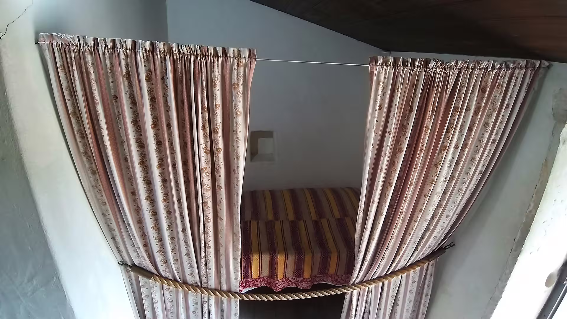 Cozy traditional bed with floral curtains in the Little Shepherds Houses on a private tour to Fátima Sanctuary, Portugal.