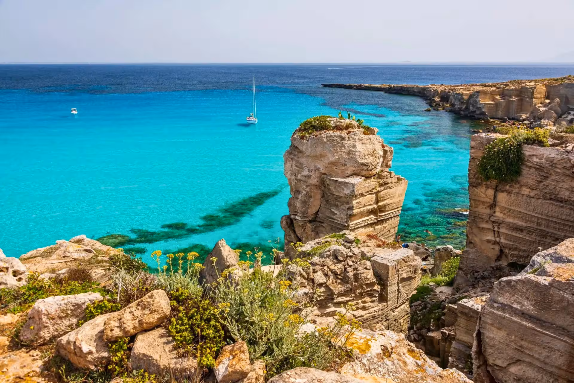 Turquoise Favignana cove with rocky cliffs and sailboat, Egadi Islands dinghy tour from Trapani