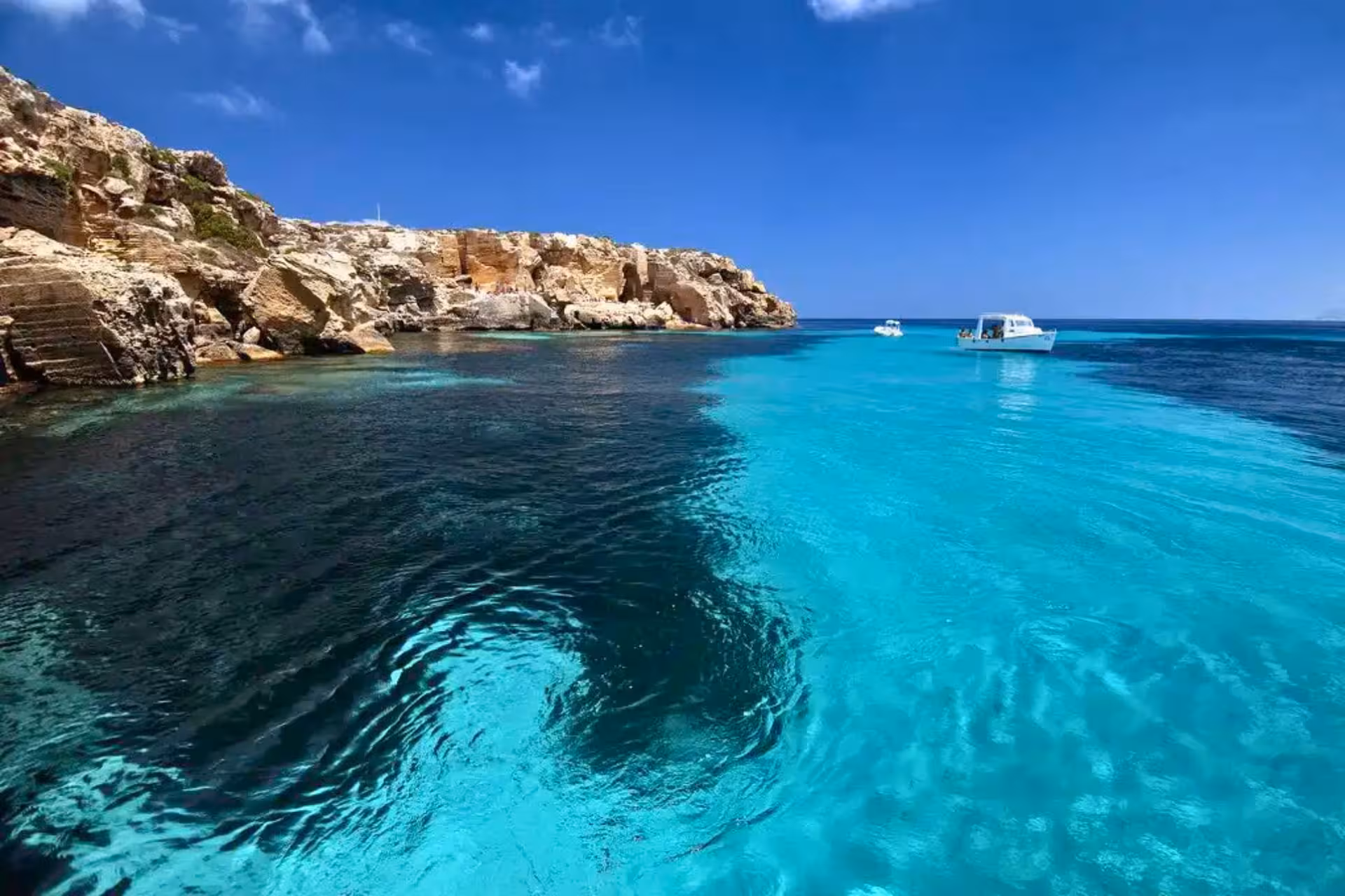 Crystal-clear Cala Rossa waters with boats off Favignana, Egadi Islands dinghy tour from Trapani incl lunch