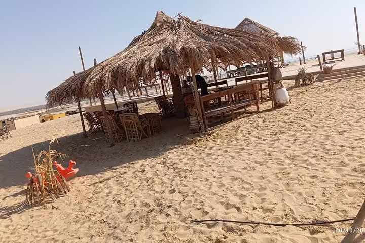 Traditional thatched hut with wooden seating on sandy landscape in Fayoum Oasis, ideal for relaxation during tours.