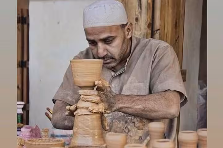 Fayoum pottery artisan shaping clay vase on wheel, authentic Egyptian craft stop on Cairo to Fayoum Oasis tour