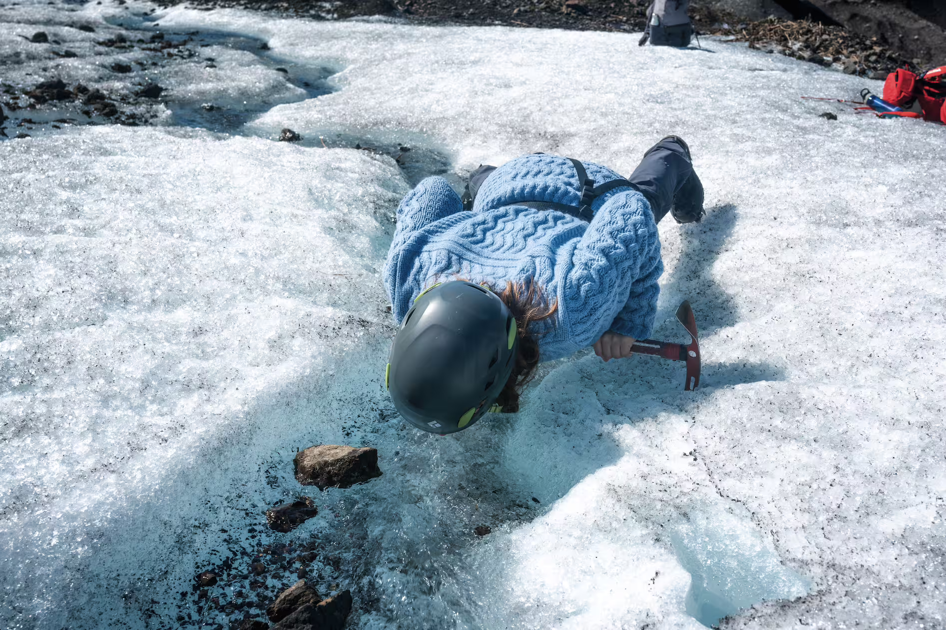 Female adventurer in helmet using ice axe while lying on Skaftafell glacier during an exciting Iceland photoshoot tour