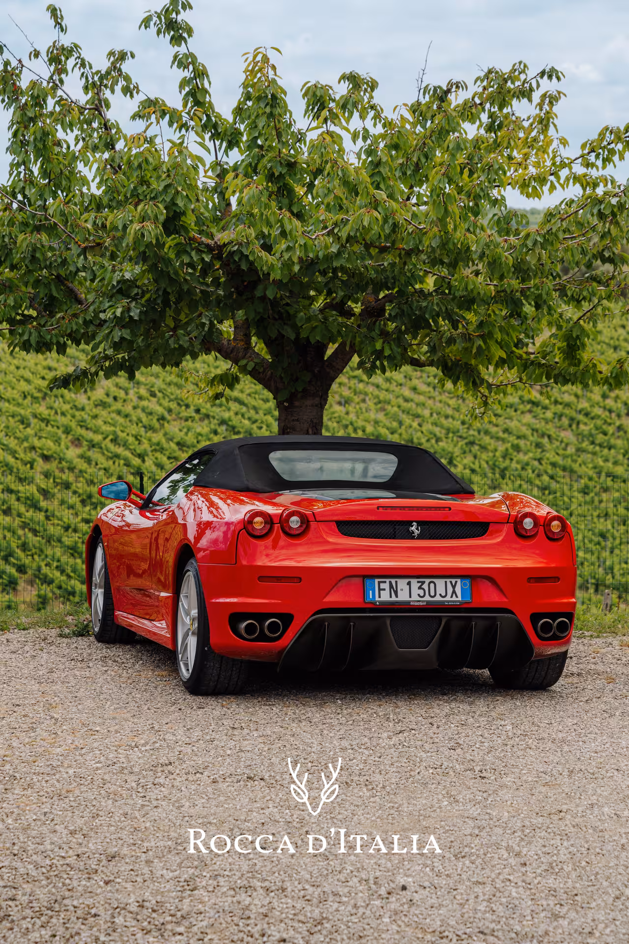 Red Ferrari F430 Spider rear view parked on gravel road surrounded by Tuscan vineyards