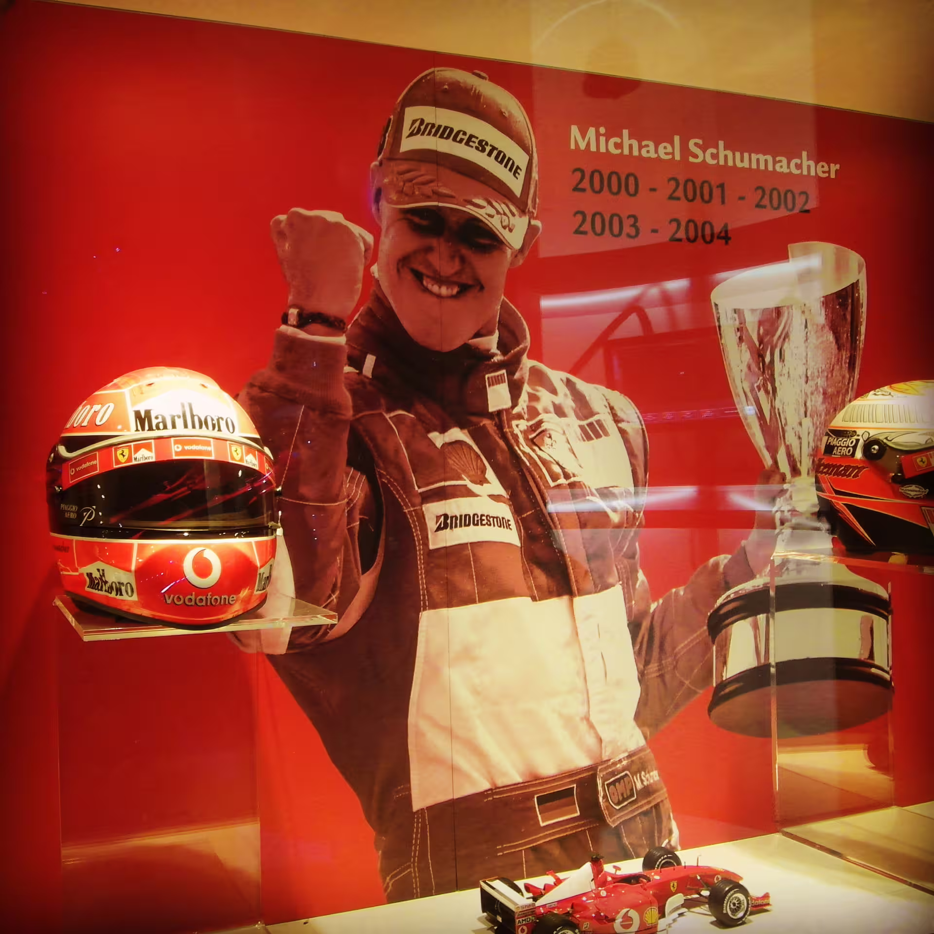 Ferrari Museum Maranello exhibit with F1 memorabilia, racing helmets and trophy on red display wall