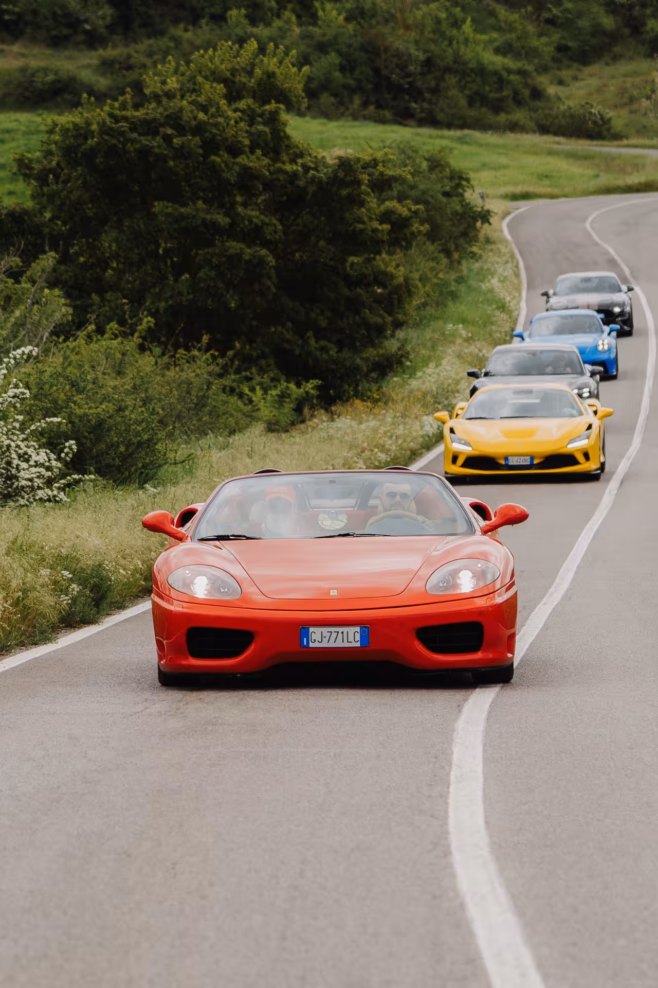 Red Ferrari 360 Spider leading a convoy of supercars on a winding Tuscan road