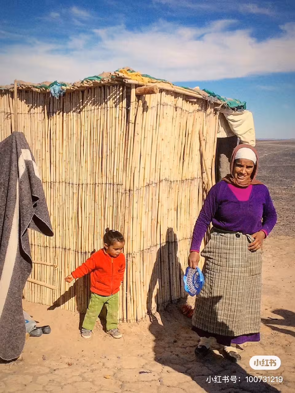 Local woman and child outside a reed hut in the desert, highlighting cultural experiences on a Fes to Errachdia tour.