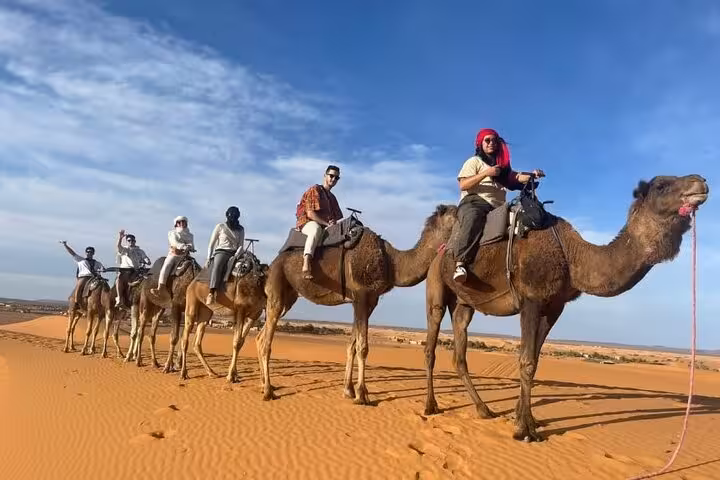 Travelers enjoy a camel ride across the golden dunes of Merzouga during a 4-day tour from Fes to Marrakech.