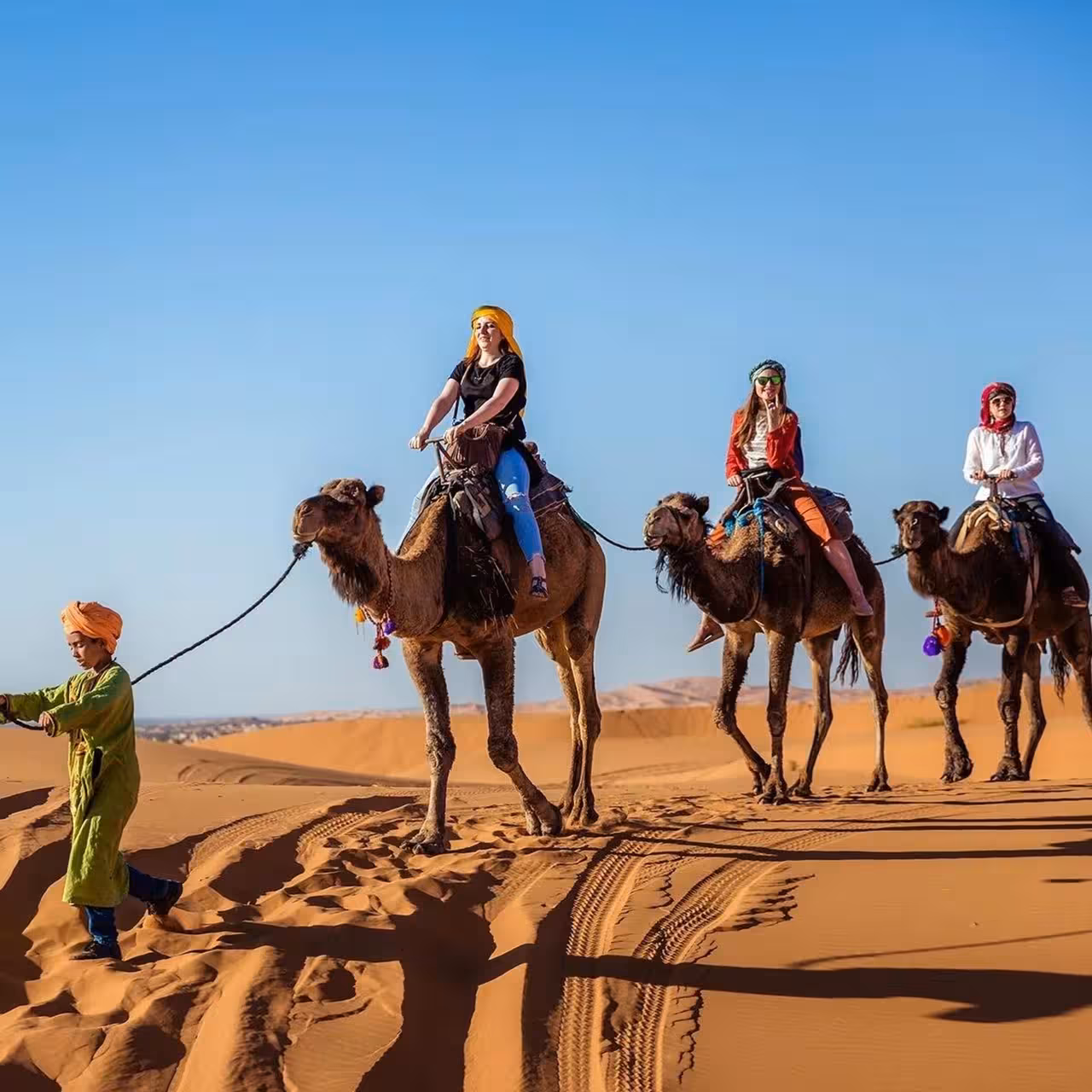 Tourists riding camels across the golden sands of Erg Chebbi, Morocco, during a private desert tour from Fes.