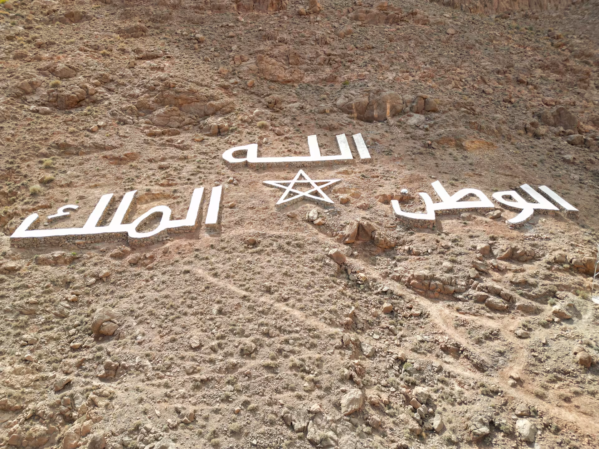 Moroccan desert landscape with Arabic script on rocky terrain, highlighting cultural landmarks on Fes to Merzouga route.