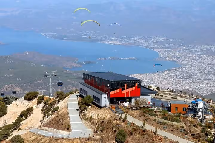 Breathtaking view of Fethiye's cable car station overlooking the bay, with paragliders soaring above the scenic landscape.