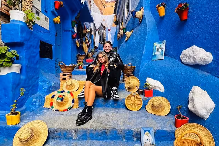 Visitors enjoy colorful, hat-adorned steps in Chefchaouen's iconic blue streets during a Fez to Chefchaouen day tour.