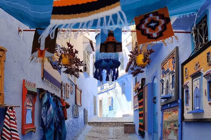 Vibrant textiles and art adorn a picturesque Chefchaouen alley, highlighting cultural stops on a Fez tour.