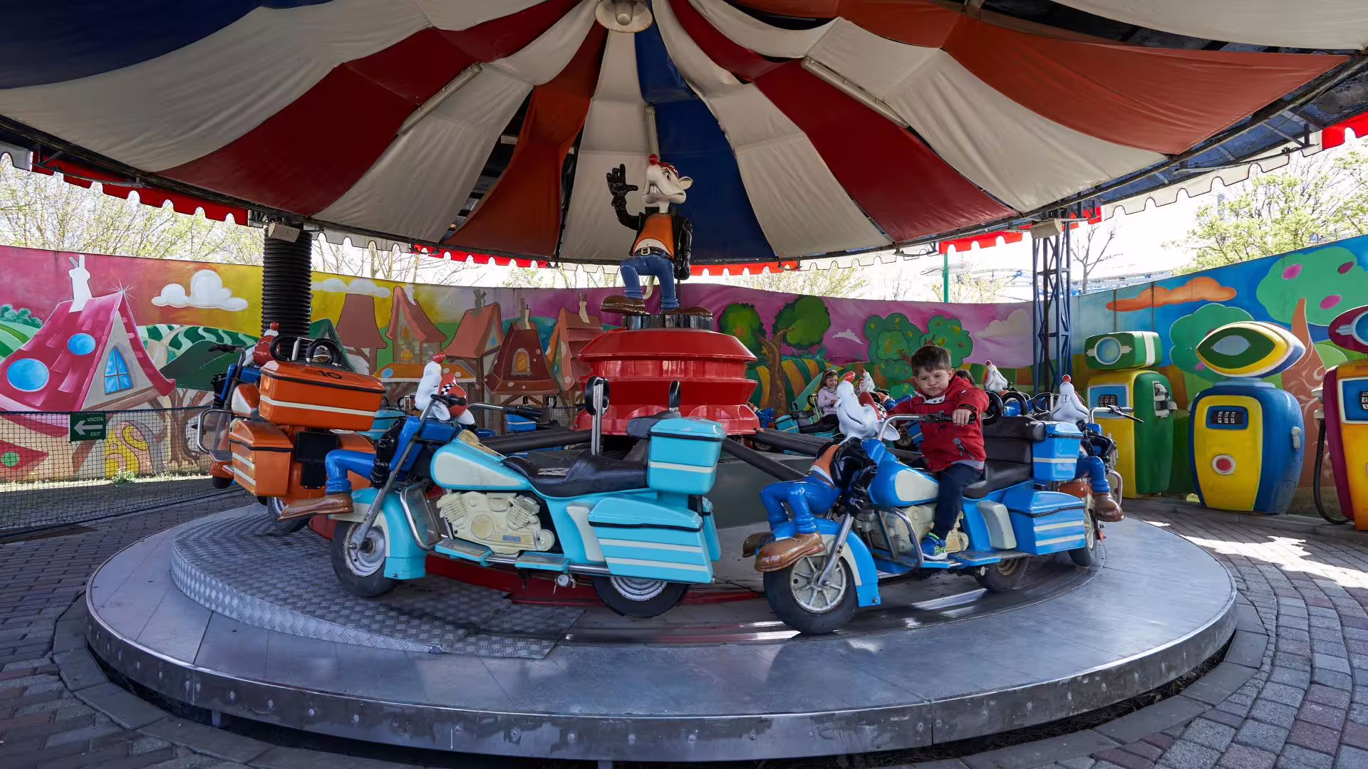Kids riding colorful motorcycle carousel at Fiabilandia amusement park in Rimini with entry ticket