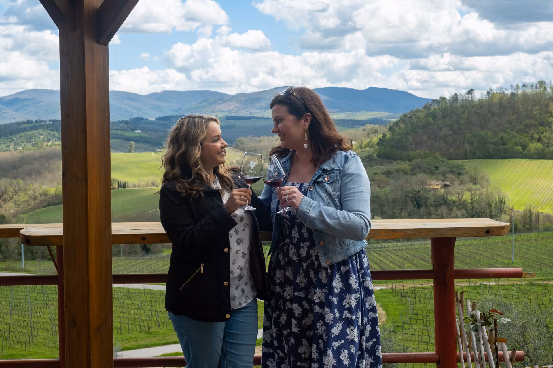 Two women enjoying a wine tasting with panoramic views of lush vineyards and rolling hills in Tuscany.