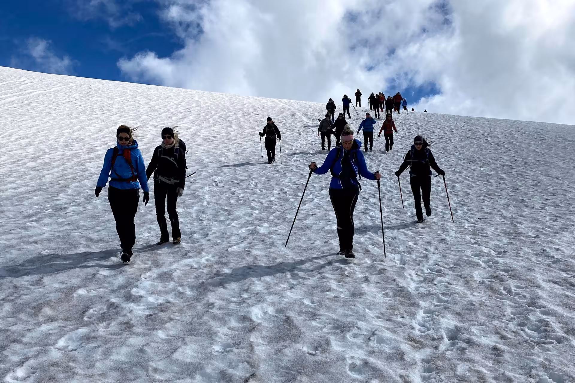 Group of hikers descending snowy Fimmvorduhals trail in Iceland using trekking poles on a sunny day